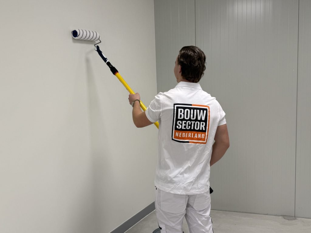 Schilder met het Bouwsector Nederland-logo op zijn rug rolt een lichte muur met een lange roller