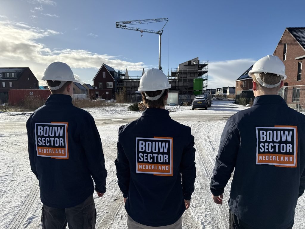 Drie vakmensen van Bouwsector Nederland met helm en bedrijfsjas bij nieuwe rijtjeshuizen in de sneeuw