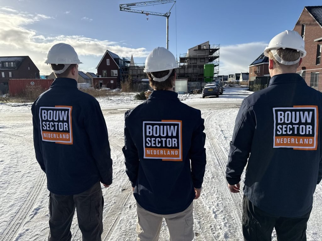 Medewerkers van Bouwsector Nederland met witte helm lopen naar een straat met woningen in aanbouw