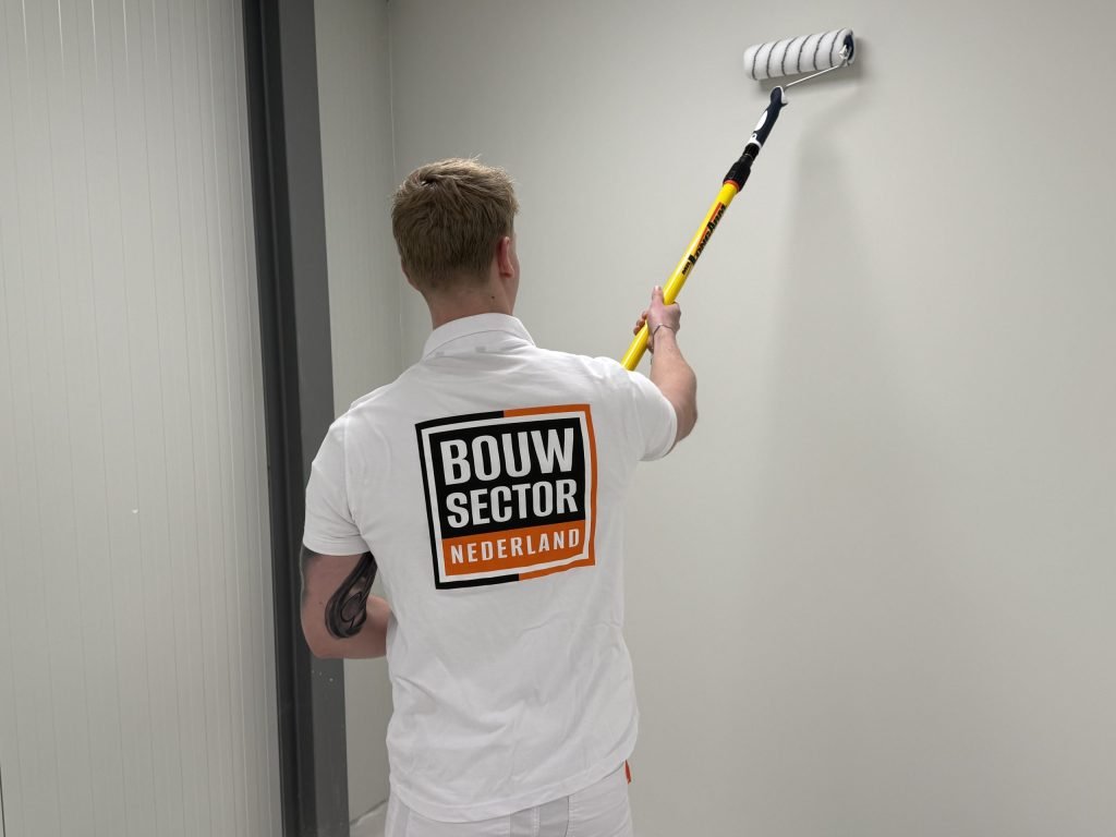 Schilder van Bouwsector Nederland rolt een lichte wand met een roller aan een gele verlengsteel